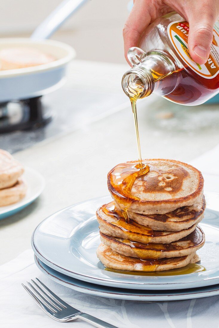A stack of pancakes being drizzled with maple syrup
