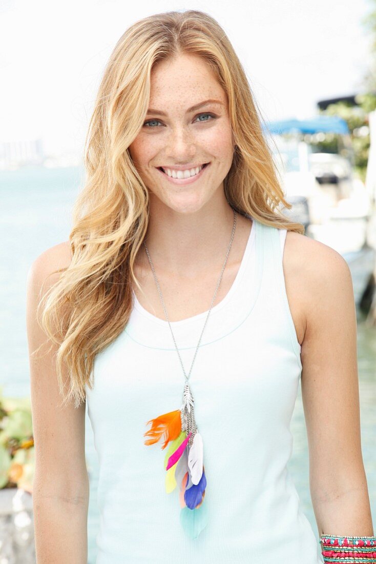 A blonde woman wearing a sleeveless top and a necklace with colourful feathers