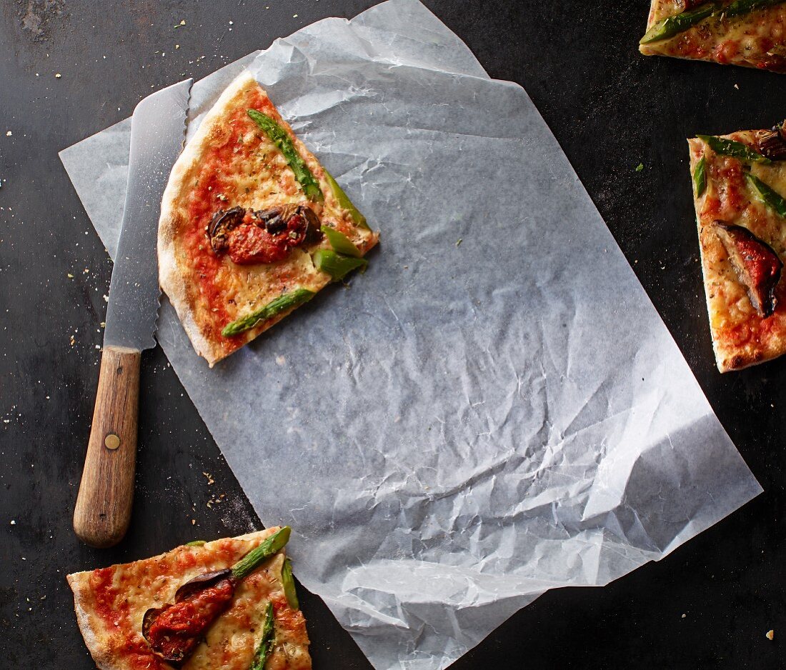 Pizza Margherita mit Spargel und Auberginen auf Papier mit Messer