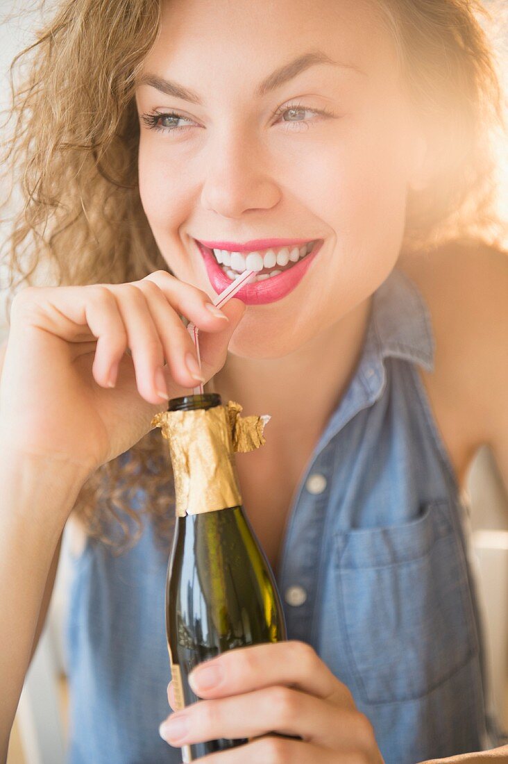 Freundliche junge Frau nippt Sekt aus einer Flasche