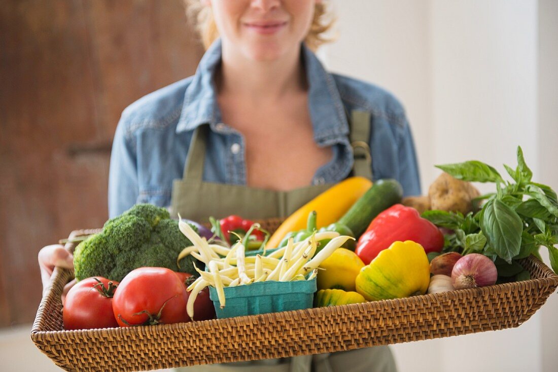 A young woman holding a wicker tray of fresh vegetables