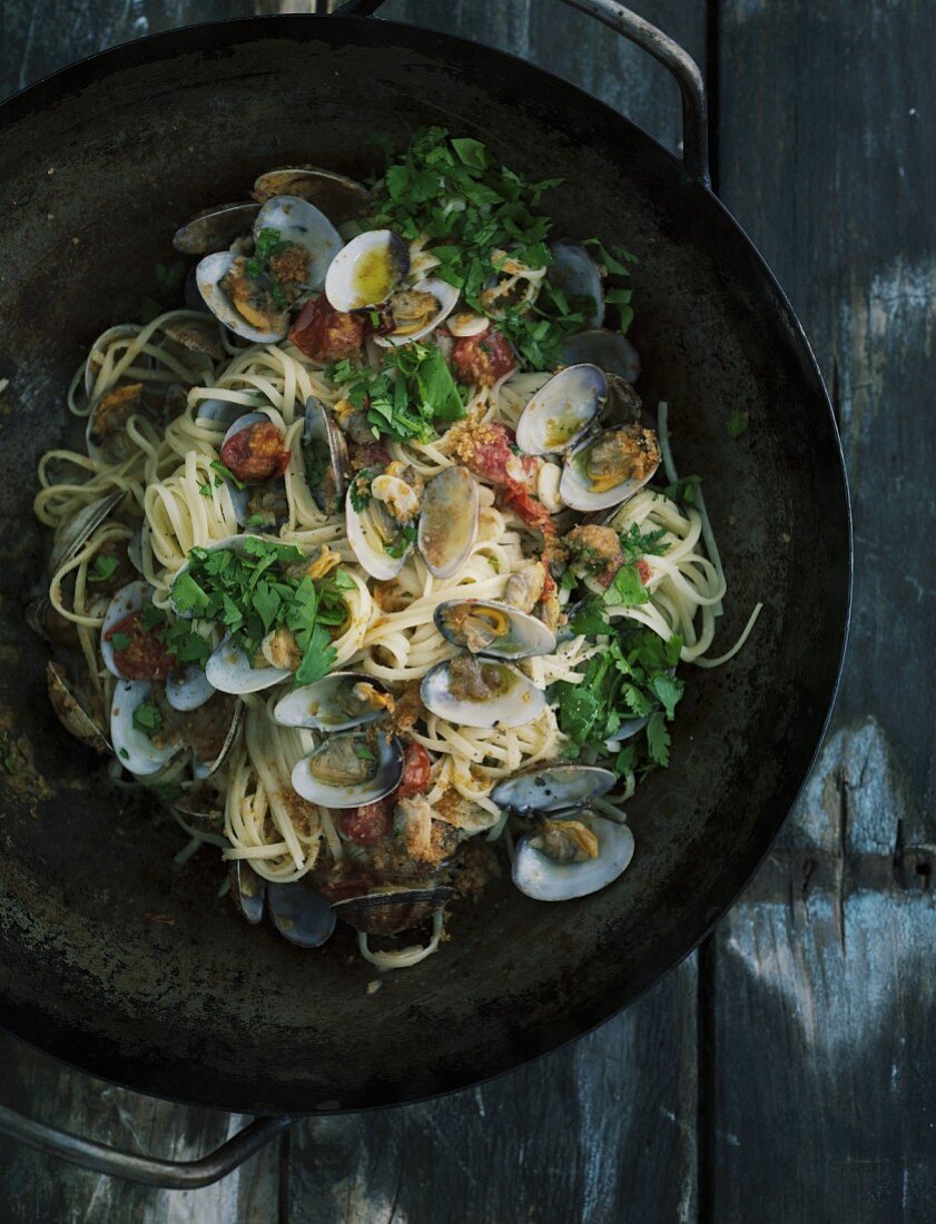 Linguine mit Venusmuscheln in Eisenpfanne auf dunklem Holztisch