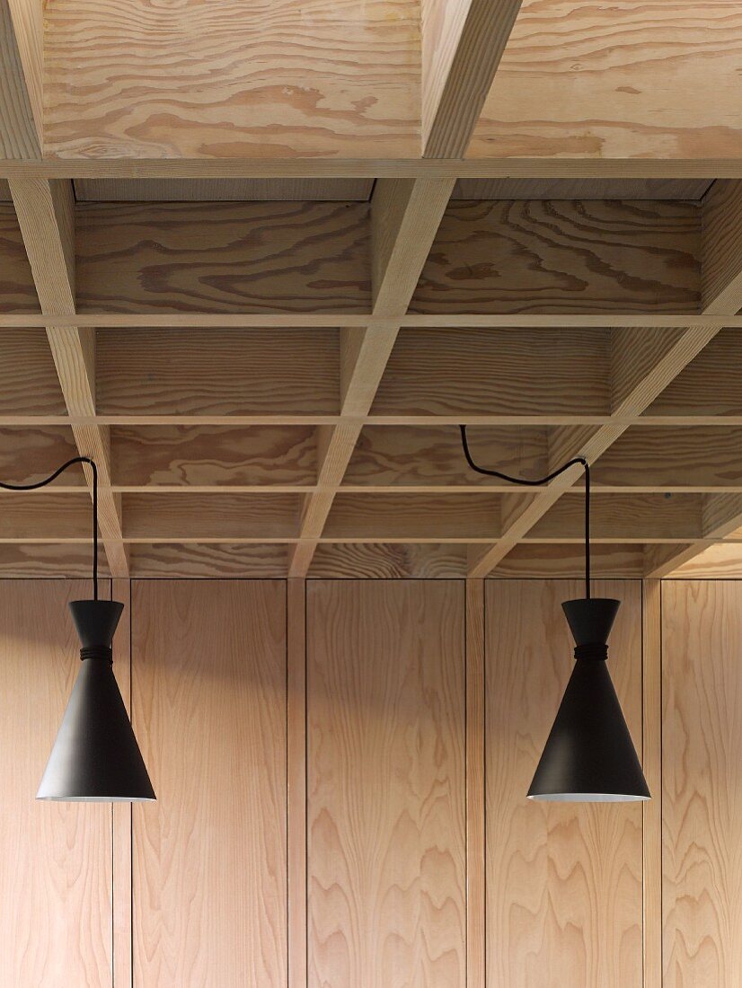 Retro pendant lamps with black metal lampshades suspended from modern coffered ceiling in pale wood