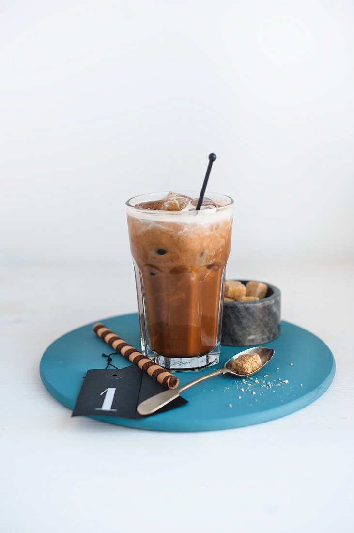 Ein Glas Haselnuss-Eiskaffee, brauner Zucker und Hippenröllchen