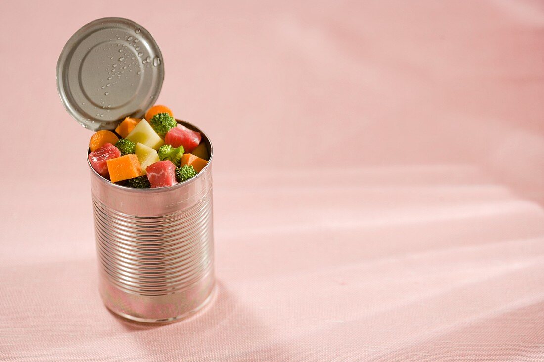 An open tin can filled with raw, diced meat and vegetables