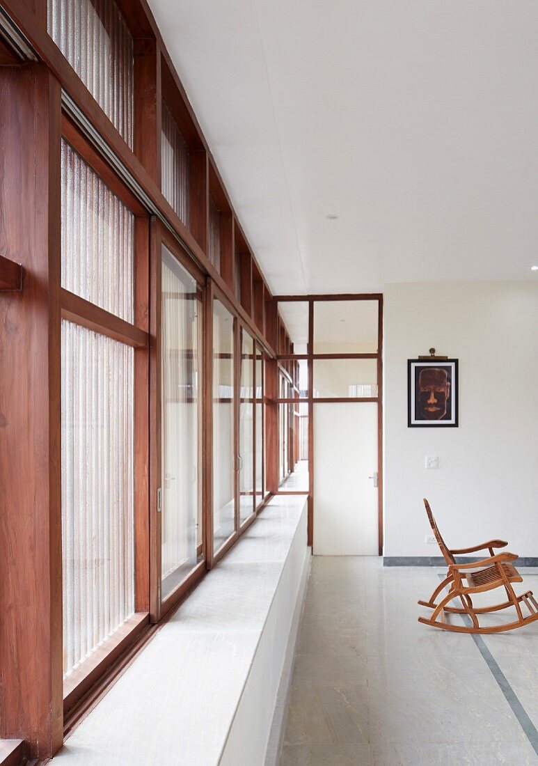Purist interior of modern, Indian house with stone floor and continuous strip of wood-framed windows