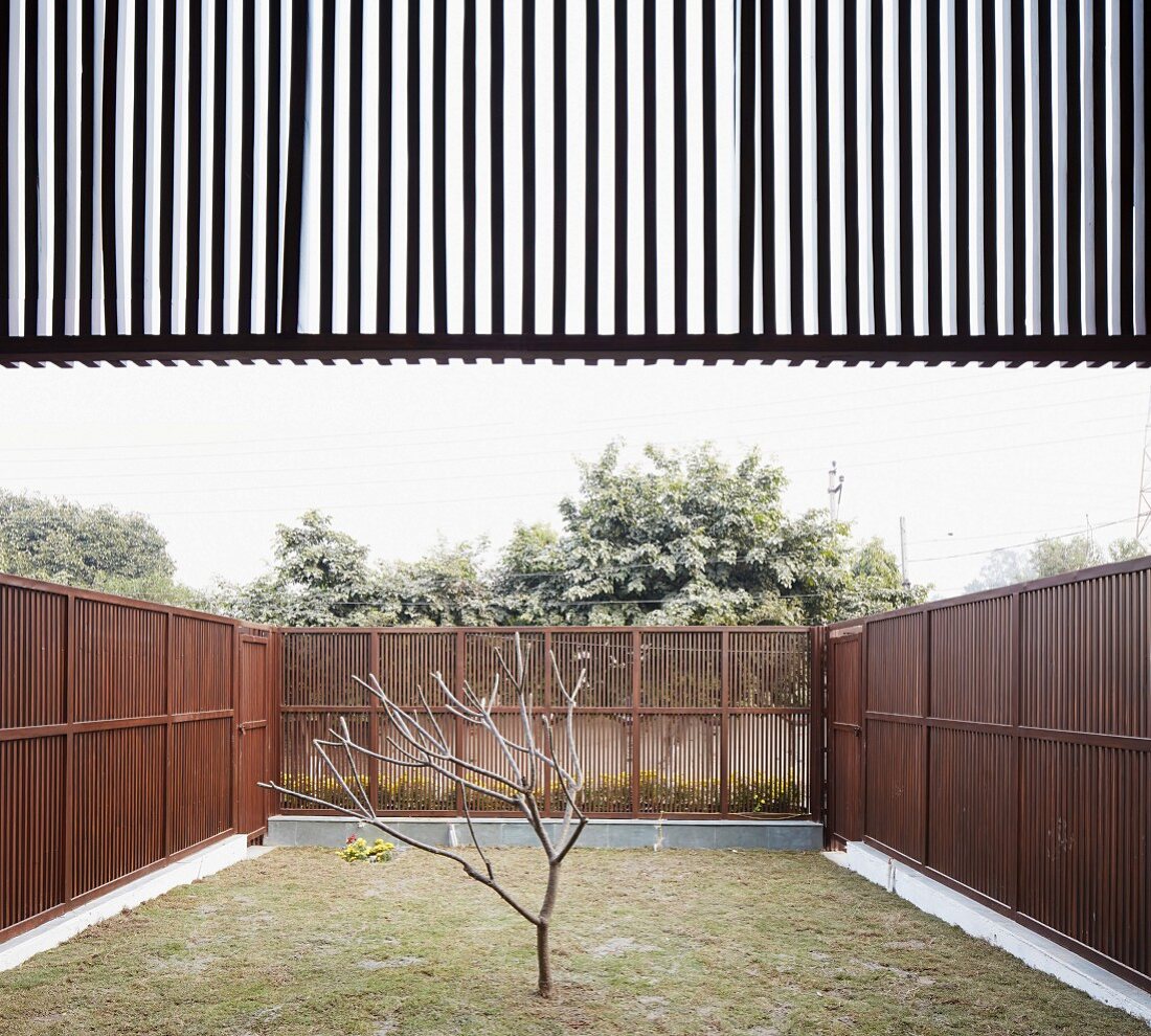 Small, austere, enclosed garden of modern Indian house with delicate wooden fences and sun screen element above