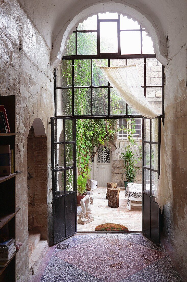 Foyer with tall, arched steel and glass door and view into courtyard of old house