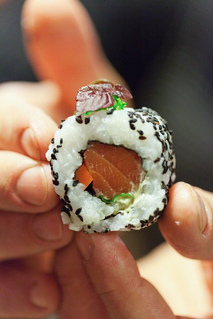 Hands holding an uramaki sushi with salmon