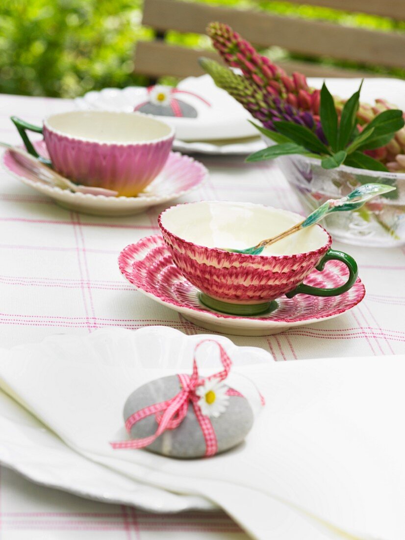 Kieselstein mit Schleife und Blüte als Serviettenbeschwerer auf sommerlichen Kaffeetisch