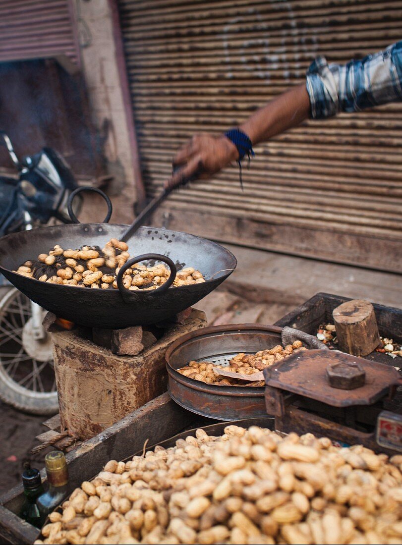 Strassenverkäufer röstet Erdnüsse auf dem Markt in Varanasi, Indien