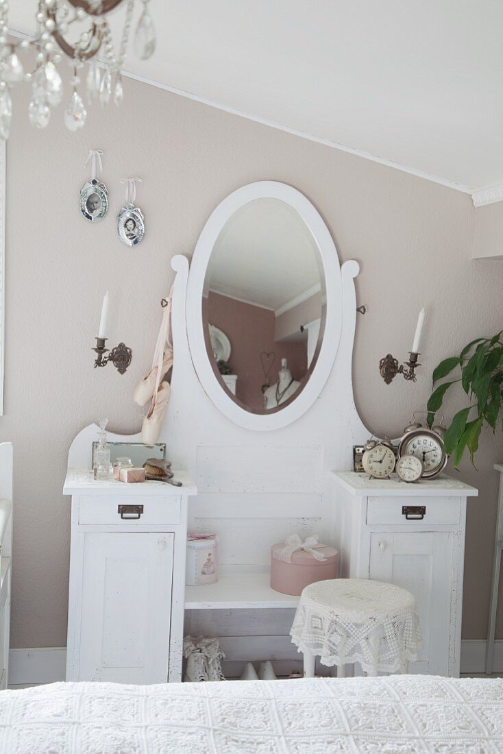 White dressing table with oval mirror against wall painted pastel grey in bedroom