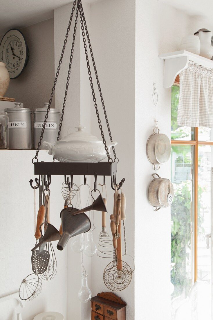 Kitchen utensils hung from metal hoop with hooks suspended from ceiling in rustic kitchen