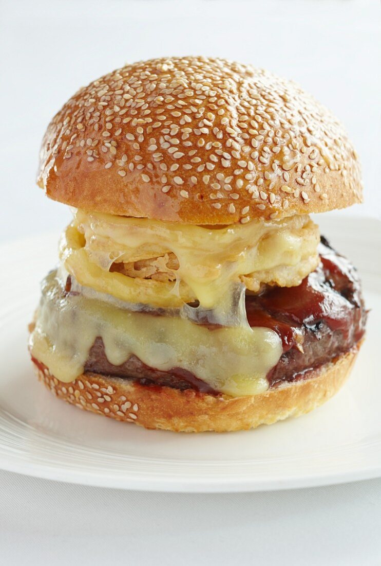 A beefburger with onion rings, melted cheese and barbeque sauce