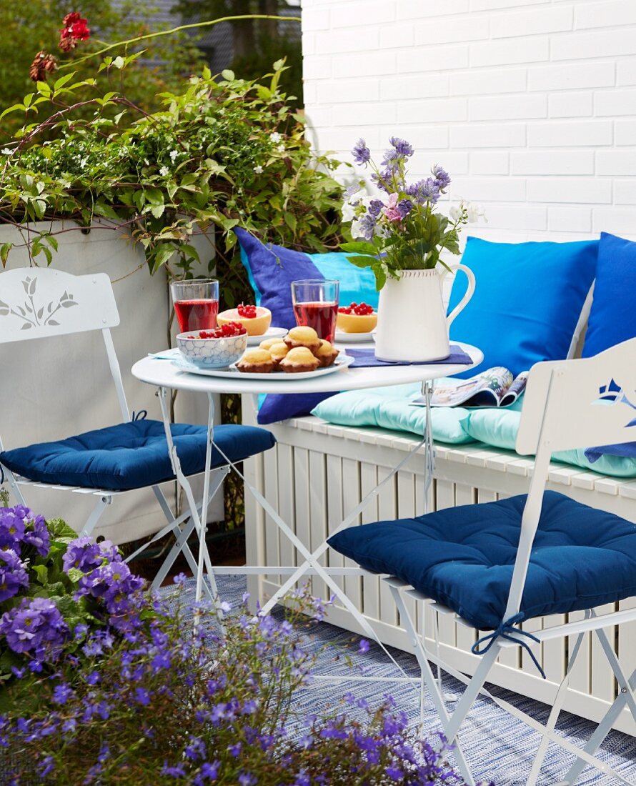 A table laid on a sunny balcony with lightweight, space-saving folding furniture and a bench chest