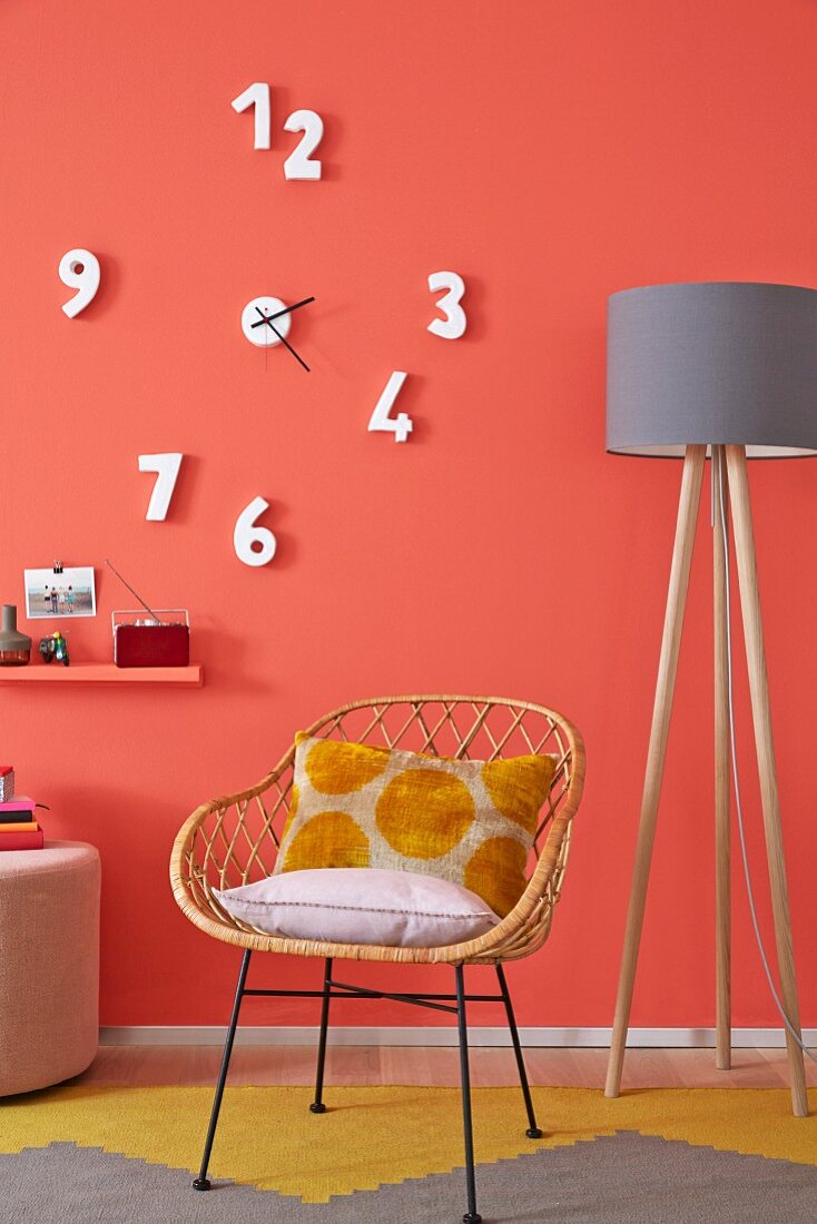 A wicker 1950s-style chair and a mustard yellow rug against a coral wall with an unconventional clock