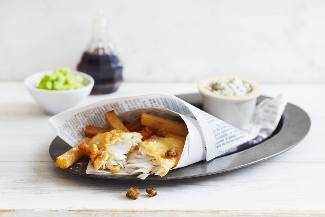 Fish and chips wrapped in newspaper served with tartare sauce and peas