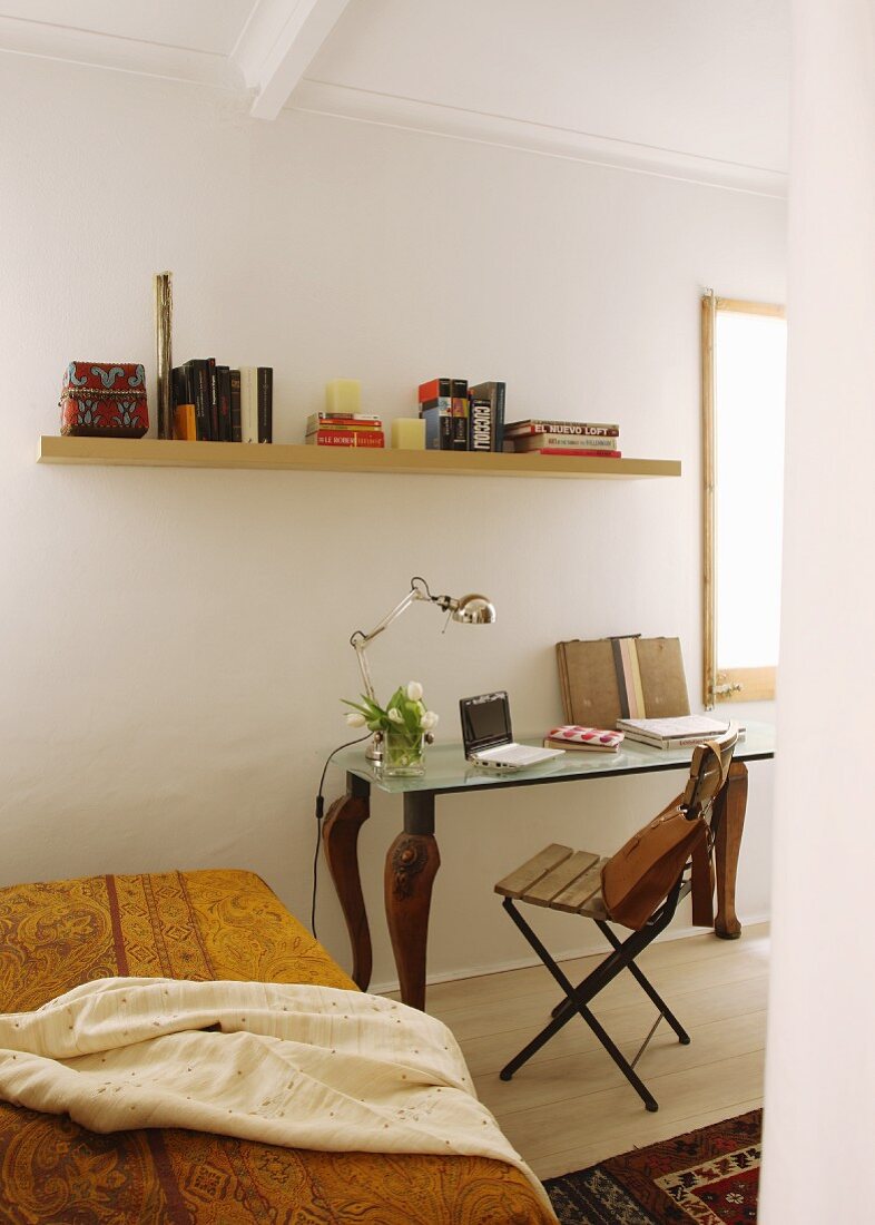 Gelbe, gemusterte Tagesdecke auf Bett, seitlich Klappstuhl und postmoderner Tisch, darüber Wandboard