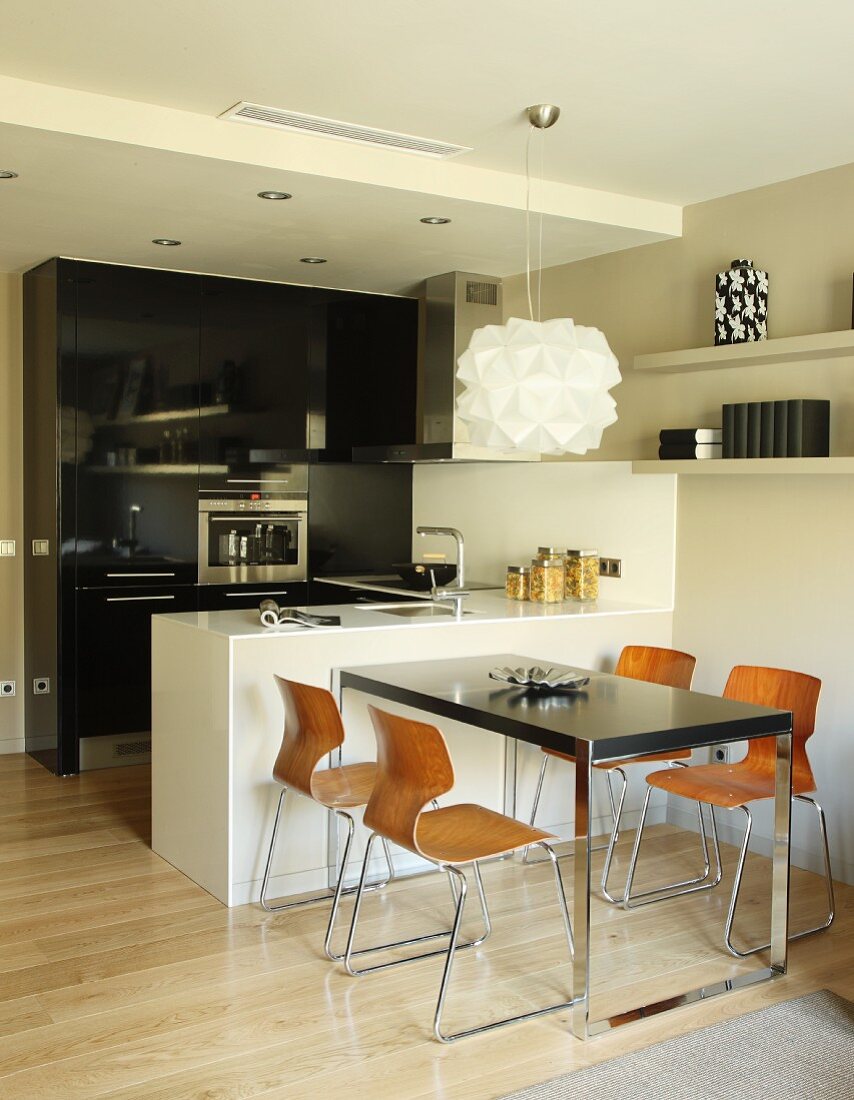 Designer pendant lamp above table and retro shell chairs next to white, monolithic counter in open-plan kitchen