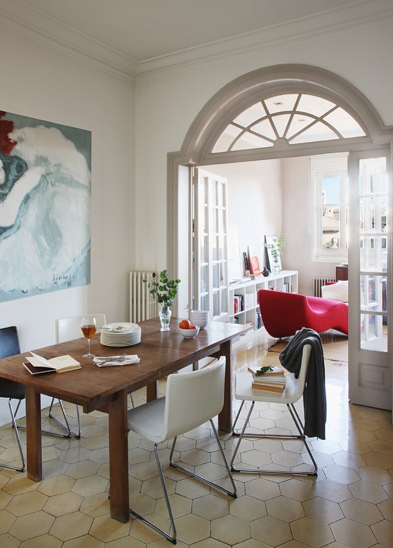 Wooden table and modern chairs with shell seats in front of open double doors with arched transom window and view of red couch in living room