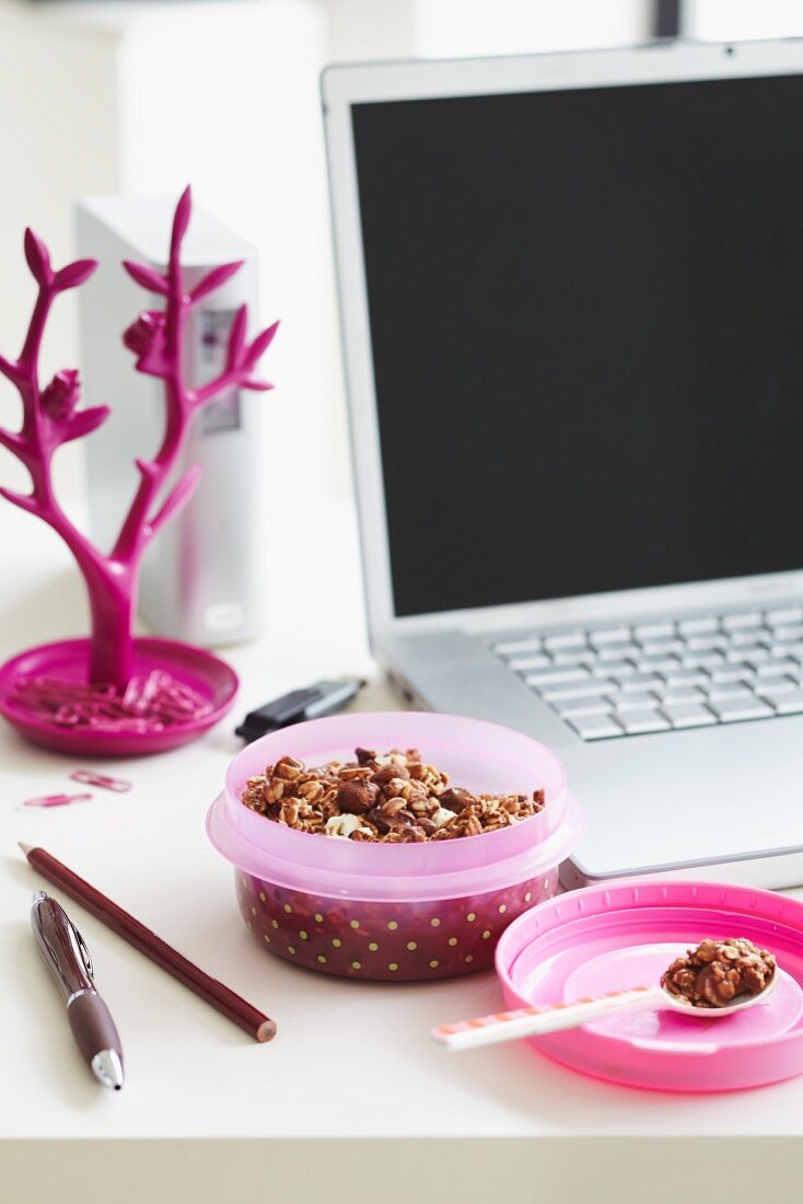 Muesli in a pink spotted Tupperware box next to a laptop