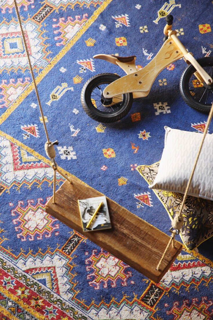 View down onto child's balance bike and simple swing above blue Oriental rug