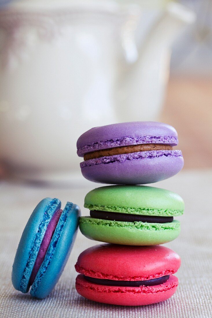 Various different coloured macaroons stacked in front of a teapot