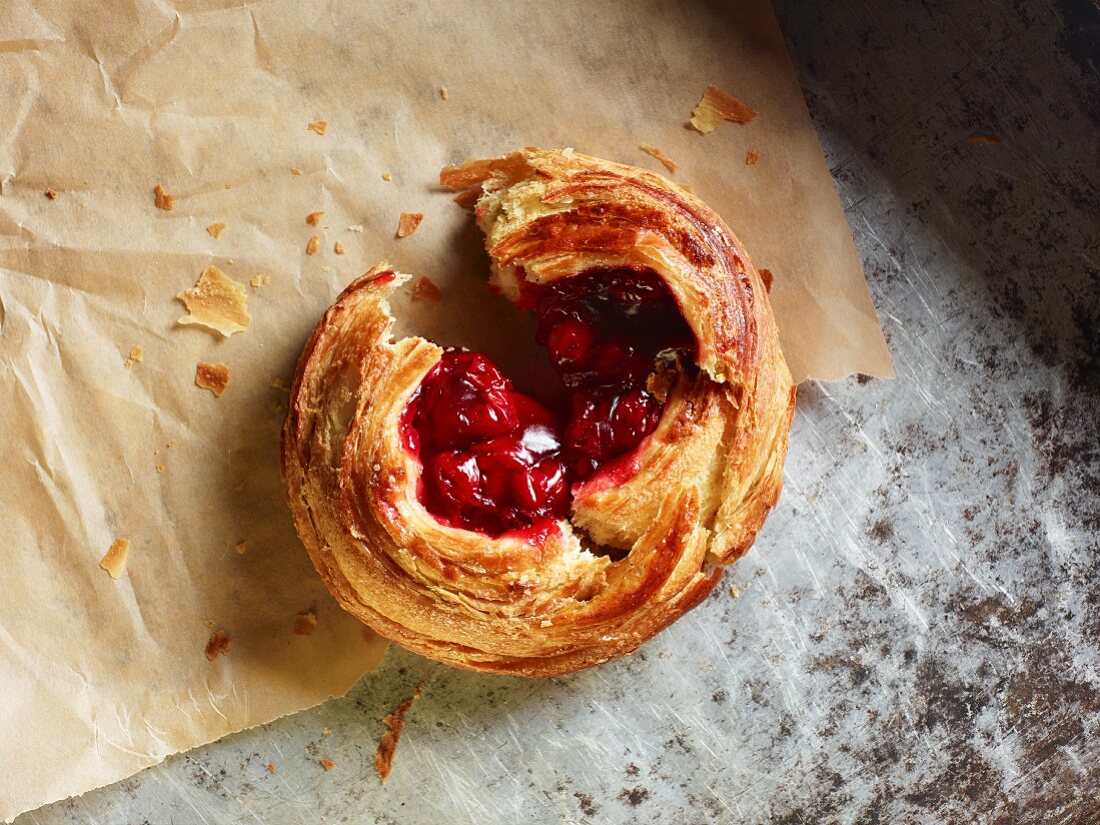 A Danish pastry with cherries on a piece of baking paper, broken