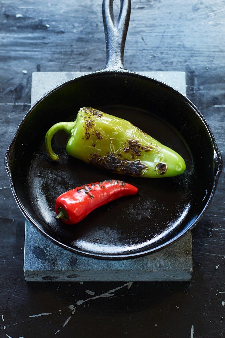 Two charred jalapeño peppers in a cast-iron pan