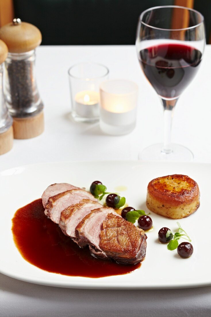 Duck breast in a pool of red wine sauce with cherries and a potato cake