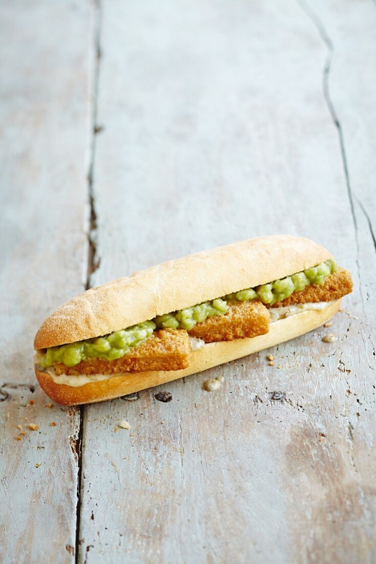 A sub sandwich with fish fingers, tartare sauce and mushy peas