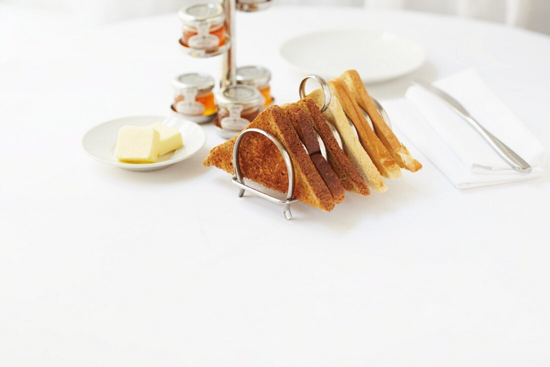 Toast in a toast rack served with butter and various jars of jam