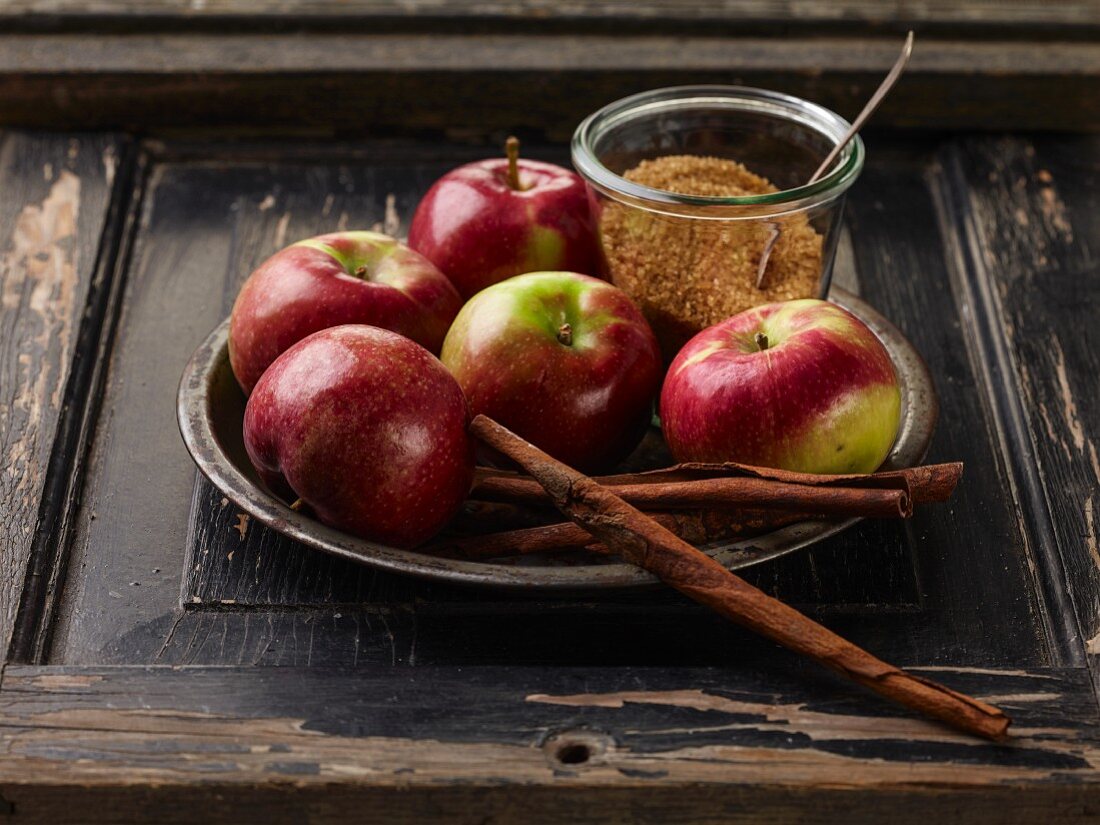 Rote Äpfel, Zimtstangen und brauner Zucker auf Metallteller