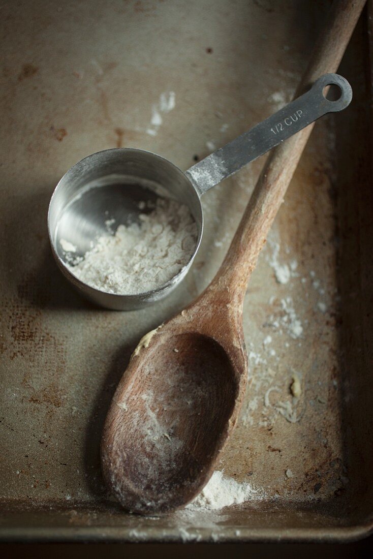 Kochlöffel und Messbecher mit Mehl auf Backblech