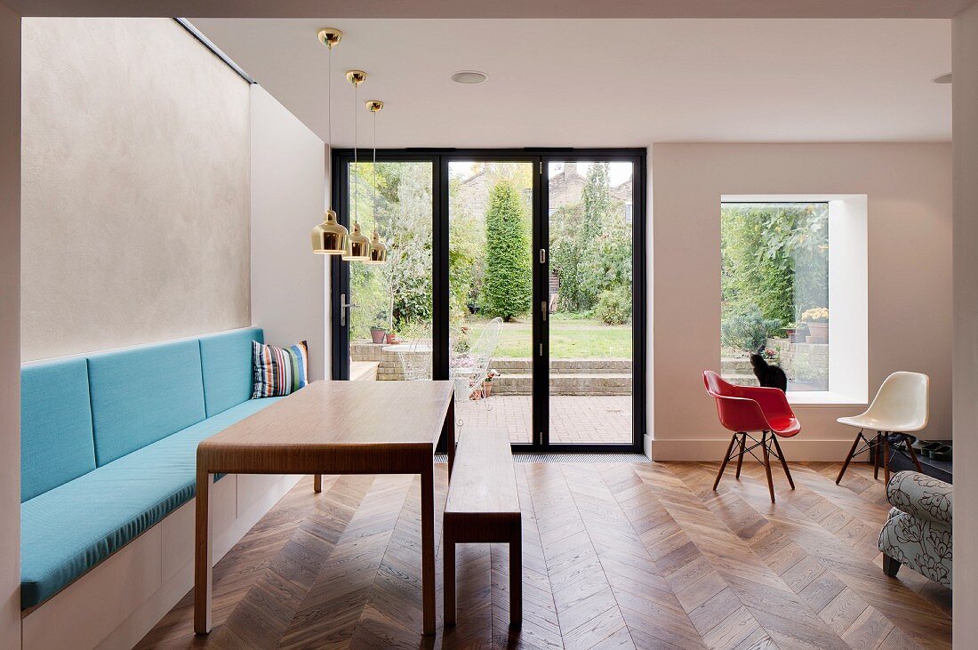 Modern table with matching bench, masonry bench with blue cushions and classic chair next to terrace doors with garden view