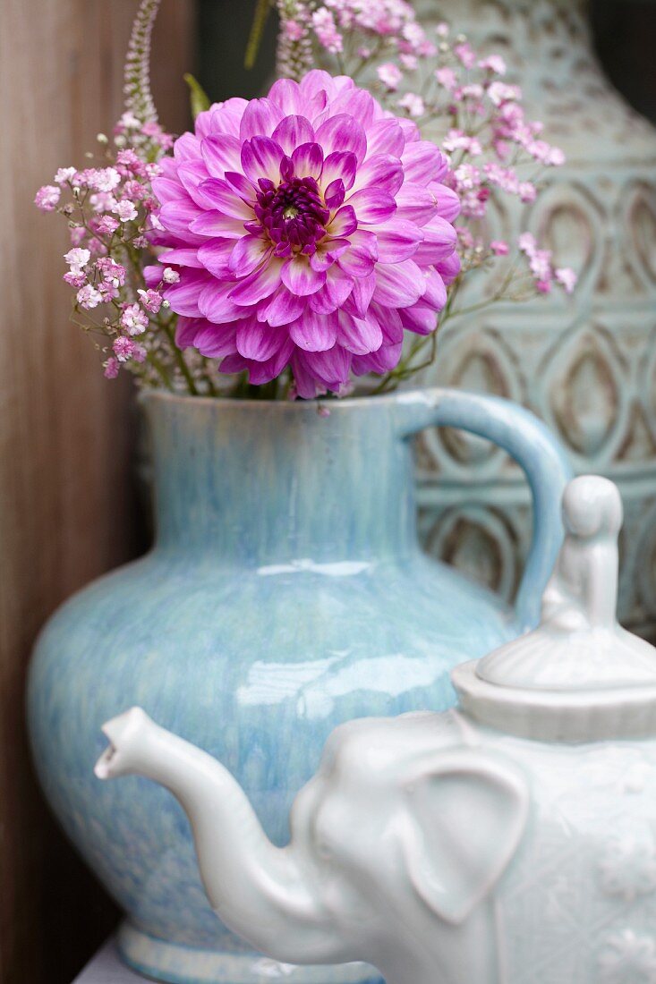 Pinkfarbene Dahlienblüte in Krugvase, davor Teekanne in Elefantenform