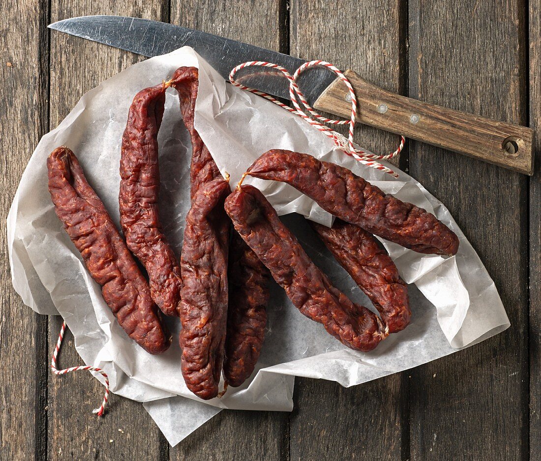 Kaminwurzen (South Tyrolean smoked sausages) on a piece of paper with a knife