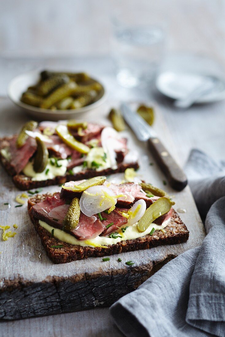 Open rye bread sandwiches topped with beef, gherkins, pickled onions and chives