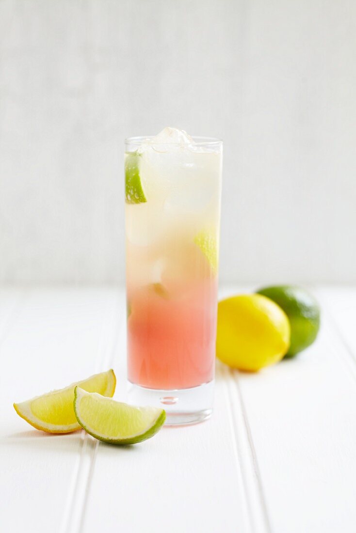 A highball glass of pink lemonade with lemons and limes