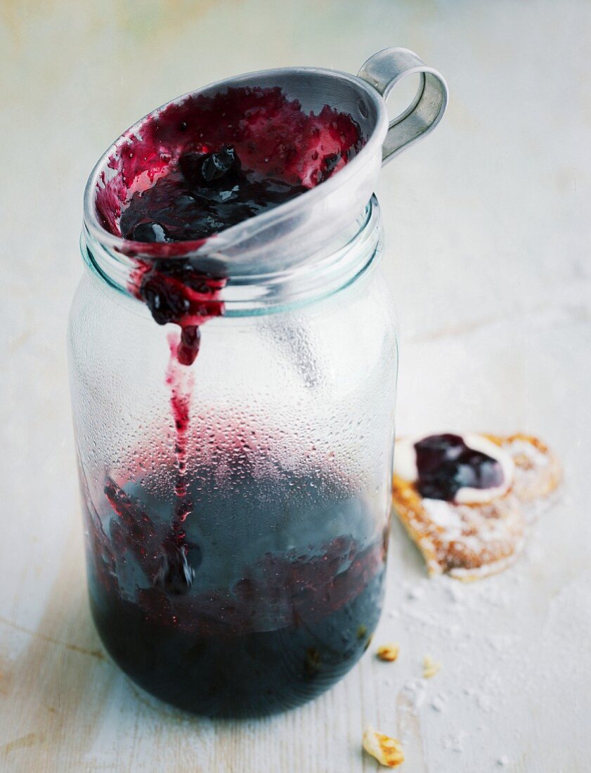 Trichter auf Marmeladenglas mit schwarzer Johannisbeerkonfitüre