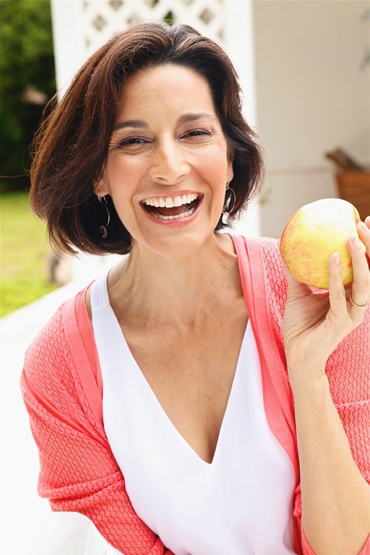 Dark-haired woman wearing top and cardigan holding apple