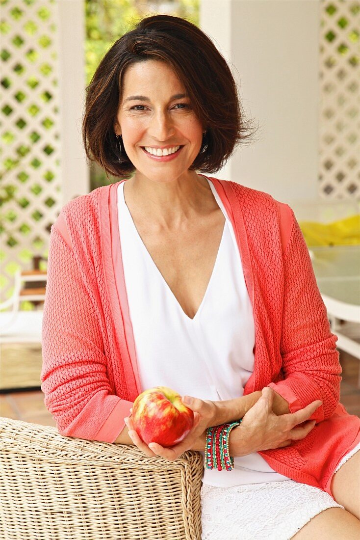 Dark-haired woman wearing top and cardigan holding apple