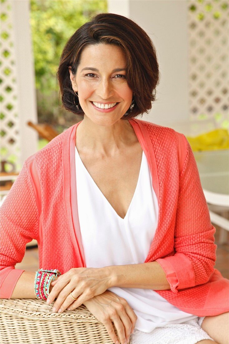 A dark-haired woman sitting in a wicker chair wearing a top and a cardigan