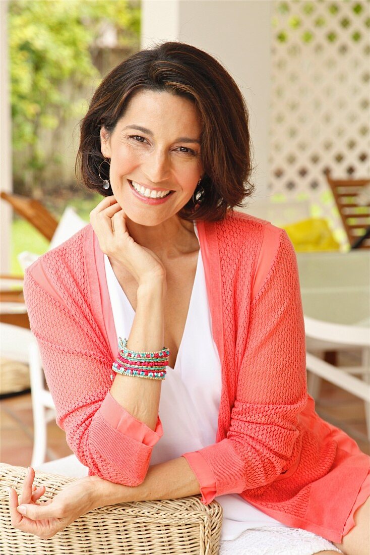 A dark-haired woman sitting in a wicker chair wearing a top and a cardigan