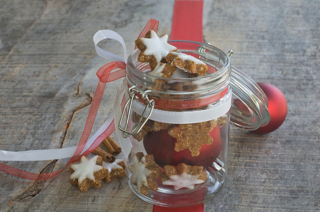 Cinnamon stars in a jar in front of Christmas tree baubles and a ribbon
