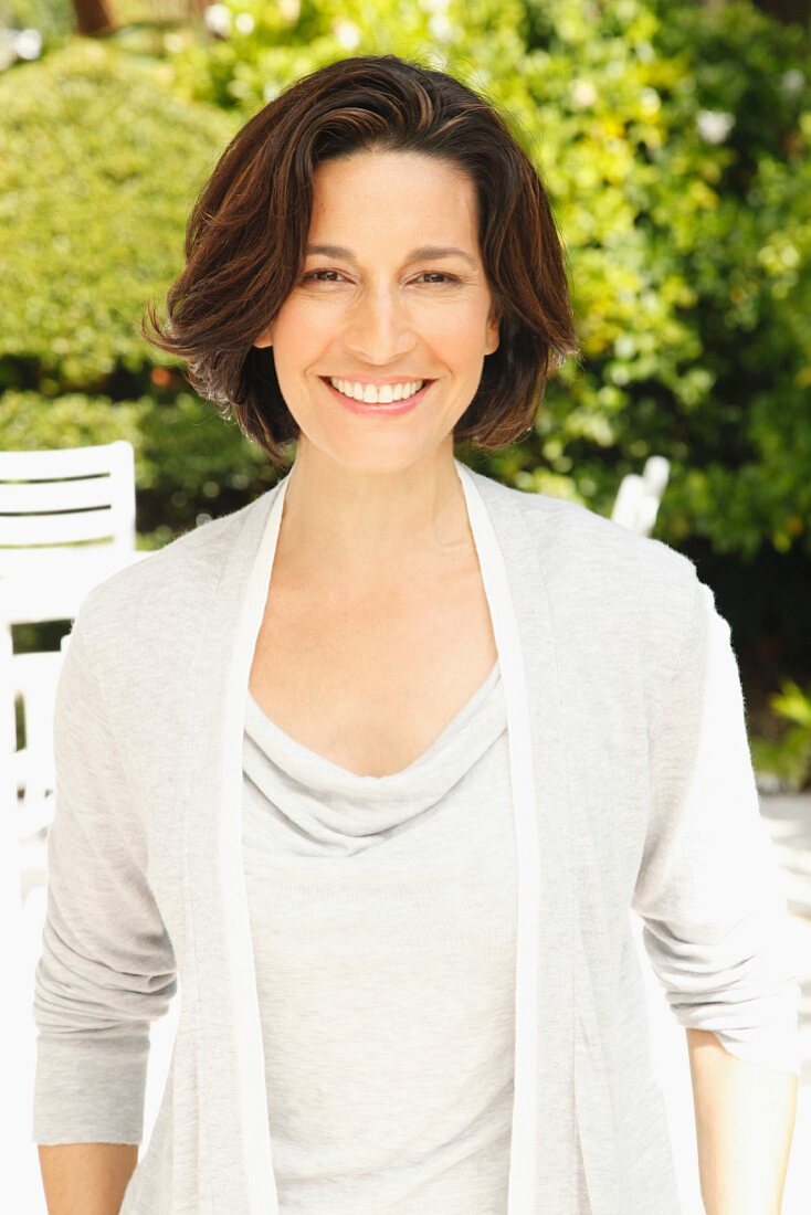 A brunette woman in a garden wearing a light grey top and a cardigan