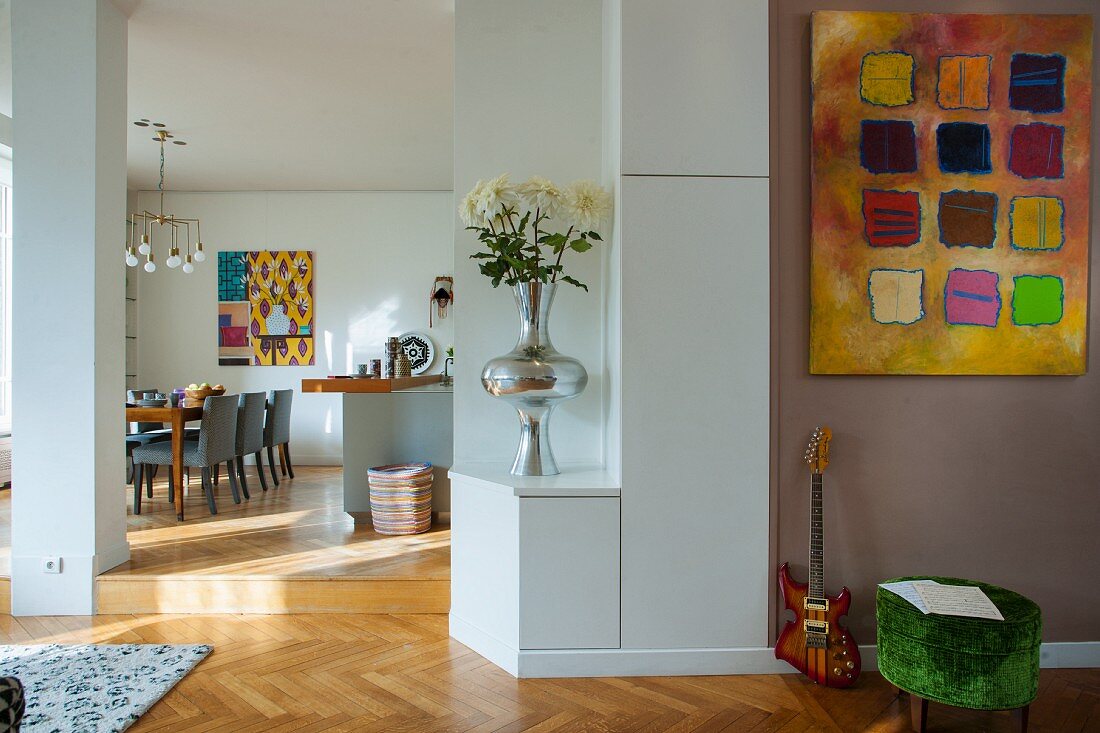 Modern artwork on grey-painted wall next to open doorway with view of dining area in background