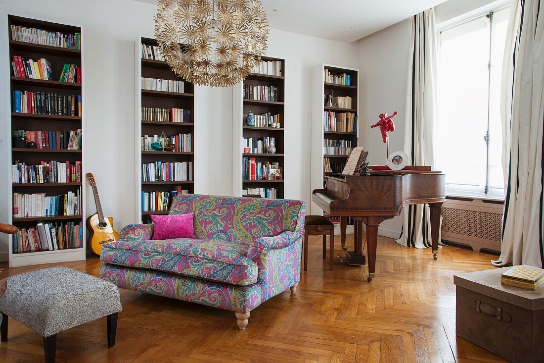 Sofa with colourful patterned cover in front of bookcases and antique piano