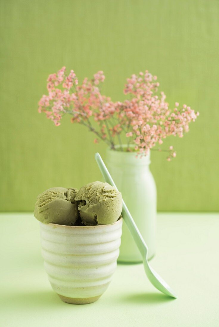 Green tea ice cream in a tub with a vase of gypsophila