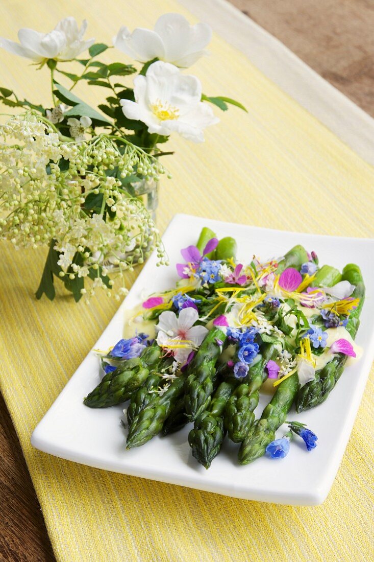 Green asparagus with a saffron sauce and edible flowers on a plate